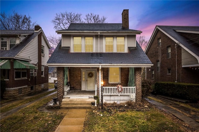 view of front of property with covered porch, brick siding, and a chimney