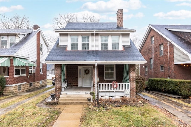 bungalow featuring covered porch, brick siding, and a chimney