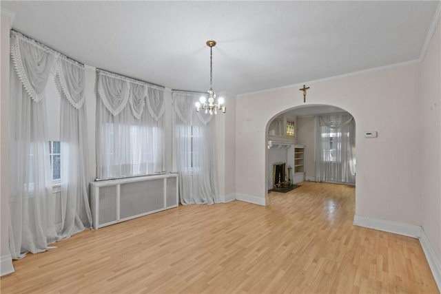 unfurnished dining area featuring arched walkways, a fireplace, radiator heating unit, and wood finished floors