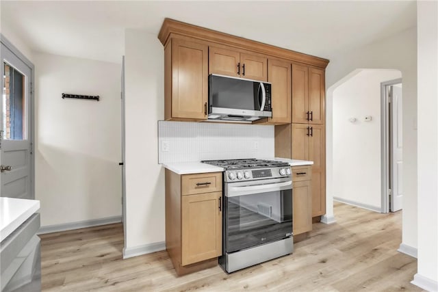 kitchen featuring arched walkways, stainless steel appliances, tasteful backsplash, light countertops, and light wood-style flooring