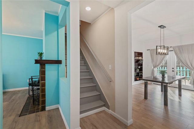 stairs featuring wood finished floors, baseboards, and a chandelier