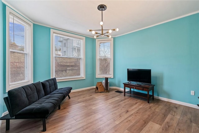 living area featuring a chandelier, ornamental molding, baseboards, and wood finished floors