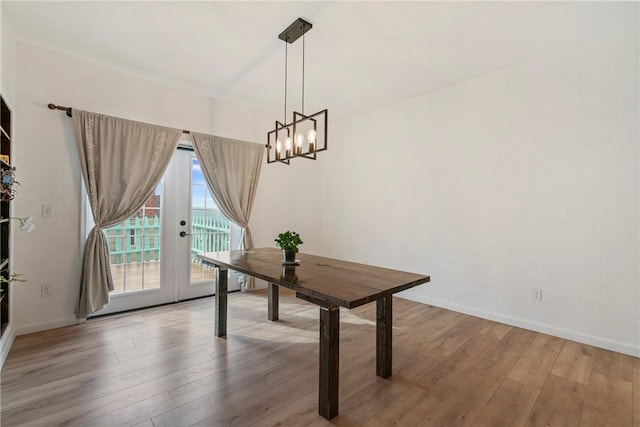 unfurnished dining area with an inviting chandelier, baseboards, brick wall, and wood finished floors