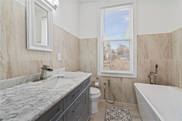 bathroom with tile walls, a soaking tub, toilet, vanity, and tile patterned floors