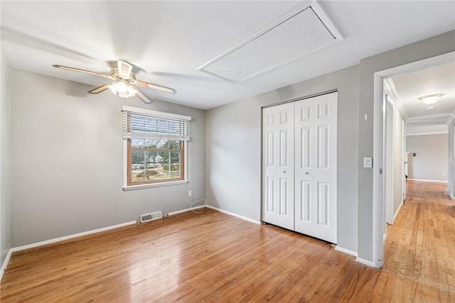 unfurnished bedroom with a closet, visible vents, attic access, light wood-type flooring, and baseboards