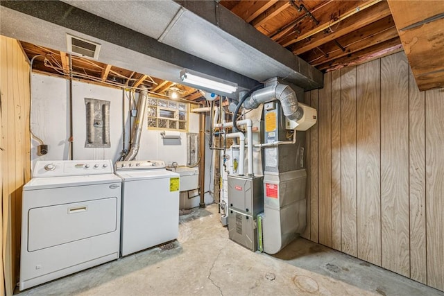 unfinished basement with wooden walls, visible vents, washing machine and clothes dryer, heating unit, and a sink