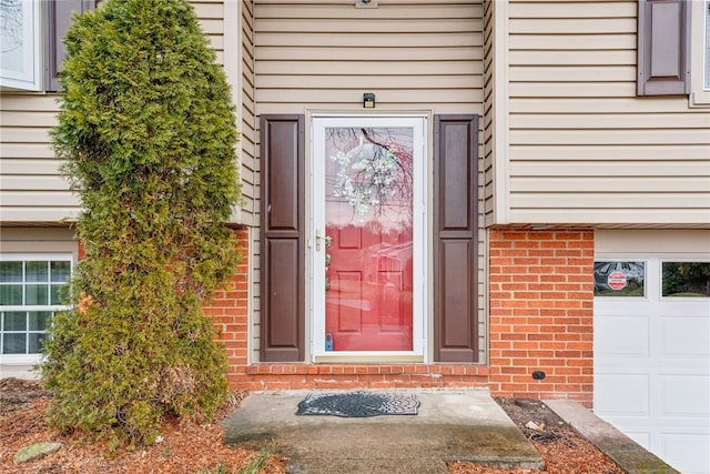 doorway to property featuring a garage and brick siding