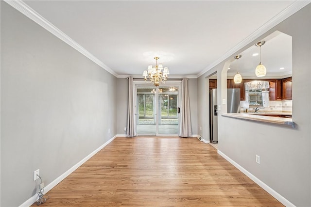 spare room with light wood-type flooring, an inviting chandelier, baseboards, and crown molding