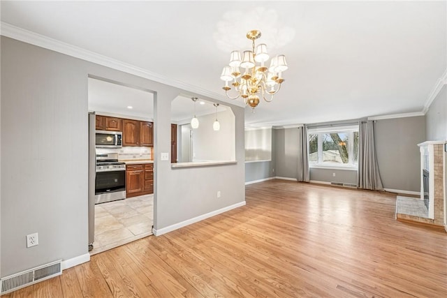 unfurnished living room with visible vents, light wood-style flooring, ornamental molding, a brick fireplace, and a chandelier