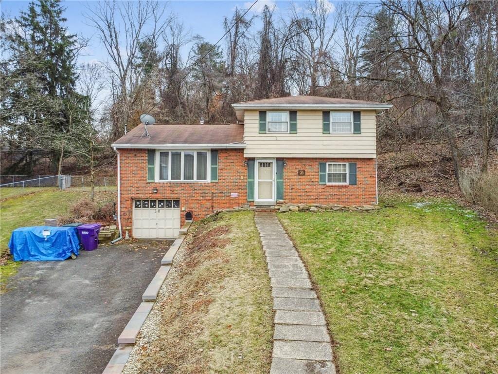 split level home featuring an attached garage, brick siding, fence, driveway, and a front lawn