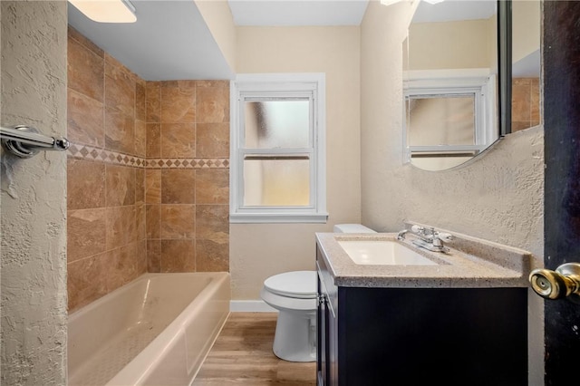 bathroom with a textured wall, toilet, vanity, wood finished floors, and baseboards