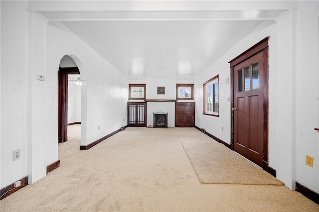 unfurnished living room featuring carpet floors, baseboards, a fireplace, and arched walkways