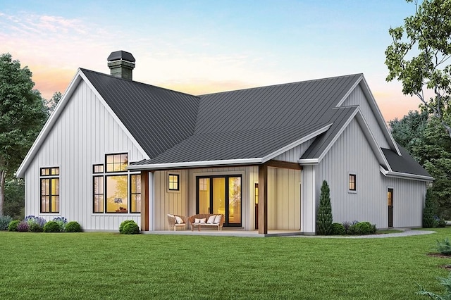 back of house at dusk featuring a chimney, a lawn, board and batten siding, a standing seam roof, and metal roof