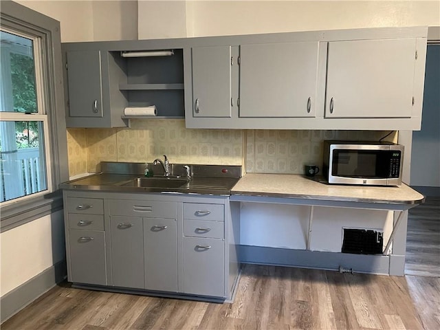 kitchen with stainless steel microwave, wood finished floors, a sink, and gray cabinetry