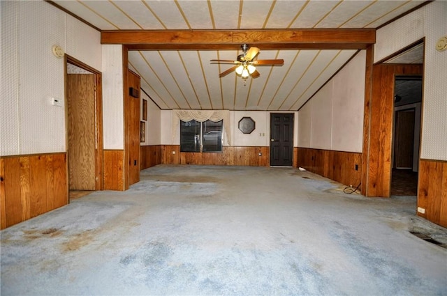 unfurnished living room featuring carpet floors, a wainscoted wall, wood walls, and lofted ceiling with beams