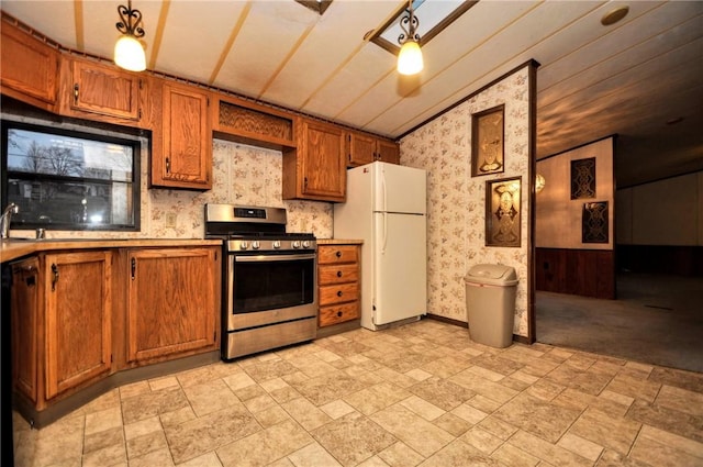 kitchen with stainless steel gas range oven, brown cabinets, freestanding refrigerator, and wallpapered walls