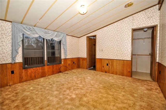 carpeted empty room with lofted ceiling, wainscoting, wooden walls, and wallpapered walls