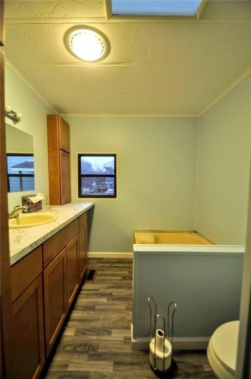 bathroom featuring crown molding, toilet, vanity, wood finished floors, and baseboards