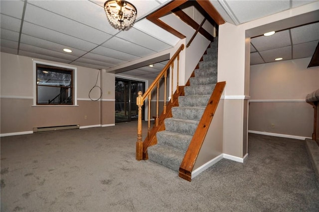 finished basement with a drop ceiling, a baseboard radiator, baseboards, stairs, and carpet