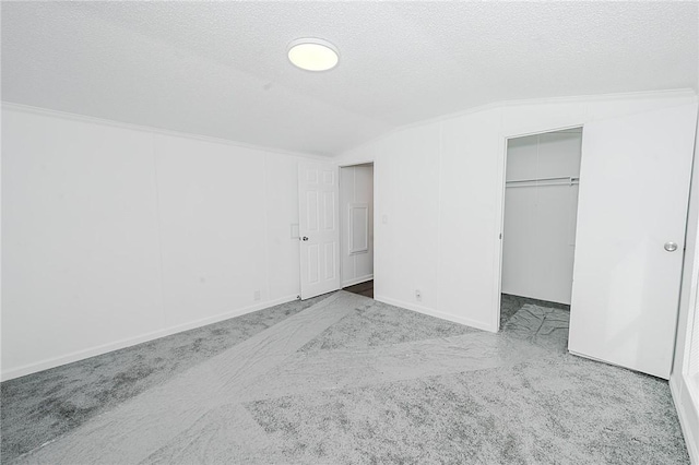 unfurnished bedroom with a walk in closet, carpet, vaulted ceiling, and a textured ceiling