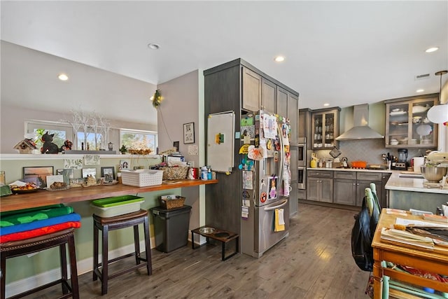 kitchen with tasteful backsplash, stainless steel appliances, wood-type flooring, light countertops, and wall chimney exhaust hood