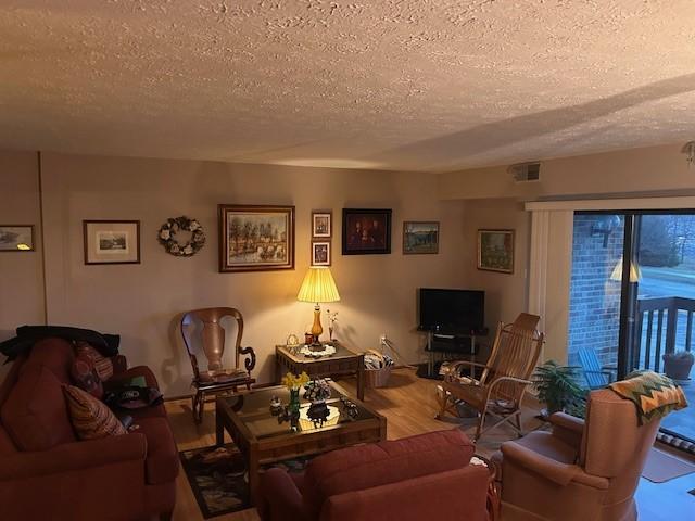 living area with visible vents, a textured ceiling, and wood finished floors