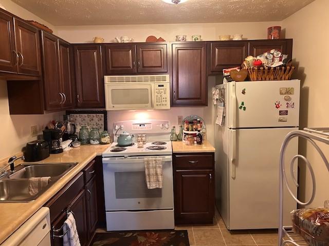 kitchen featuring white appliances, dark brown cabinets, light countertops, and a sink