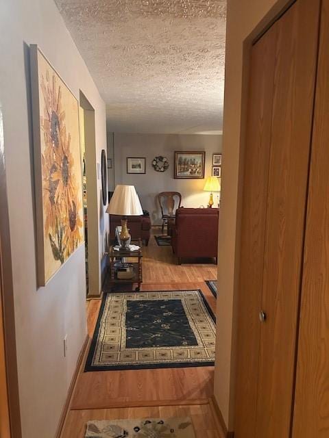 hall featuring a textured ceiling, baseboards, and wood finished floors