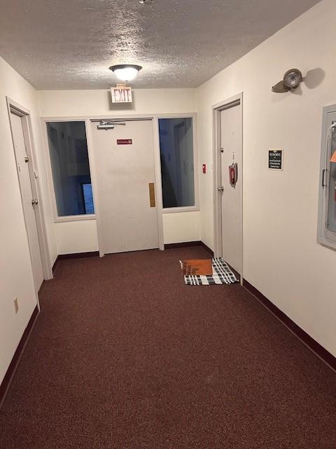 hall with baseboards, dark carpet, and a textured ceiling