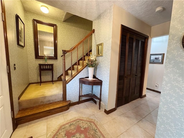 hallway with a textured ceiling, baseboards, stairs, and wallpapered walls