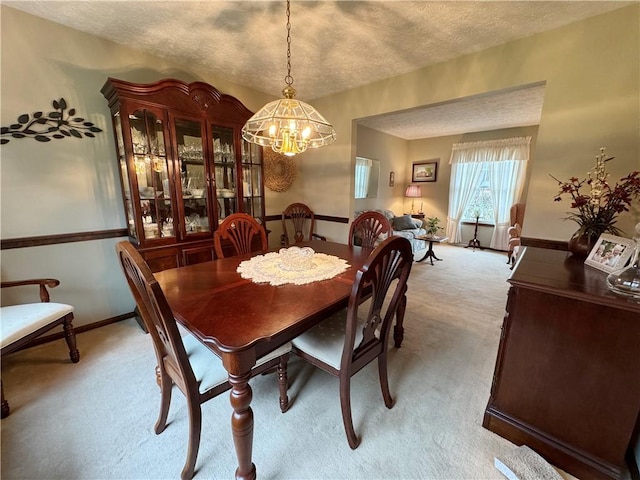 dining area featuring light carpet, an inviting chandelier, baseboards, and a textured ceiling