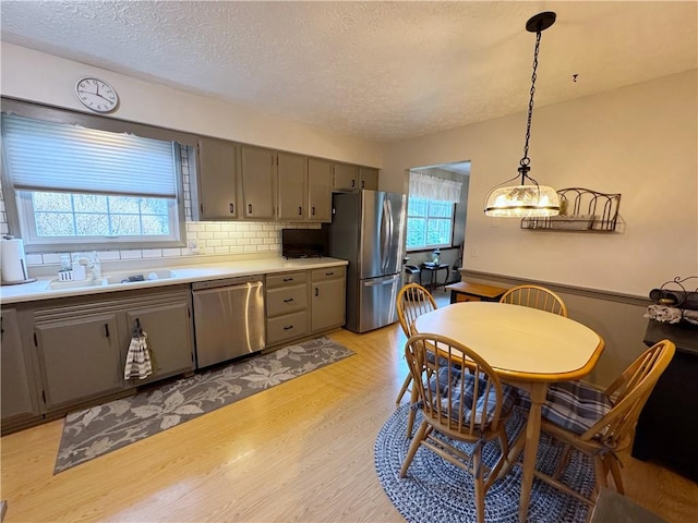 kitchen featuring a sink, appliances with stainless steel finishes, light wood-type flooring, gray cabinets, and tasteful backsplash