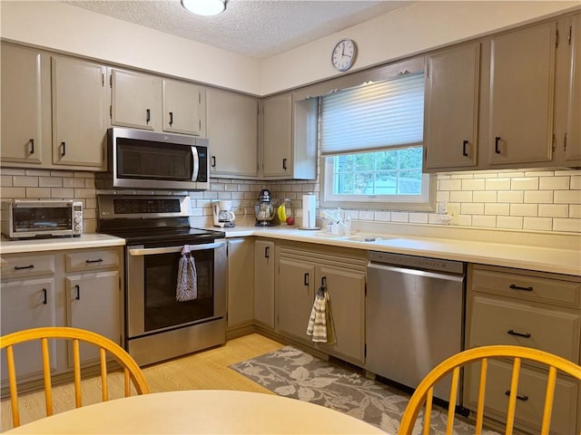 kitchen featuring a toaster, light wood-style flooring, appliances with stainless steel finishes, gray cabinets, and a sink