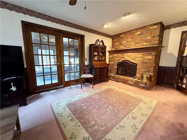 living room featuring a wainscoted wall, carpet, a textured ceiling, french doors, and a brick fireplace