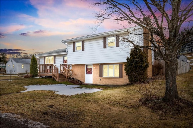 split level home featuring a yard, brick siding, fence, and a wooden deck