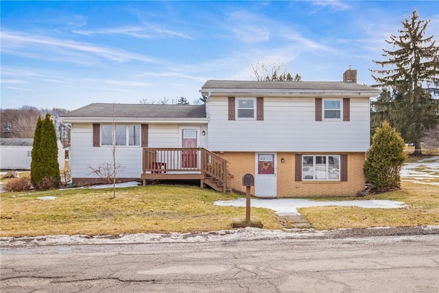 tri-level home with brick siding, a chimney, a front yard, and a wooden deck