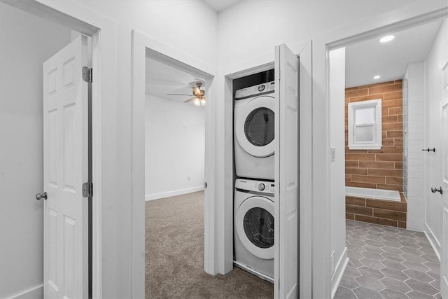 laundry area featuring laundry area, carpet floors, a ceiling fan, stacked washing maching and dryer, and tile patterned floors