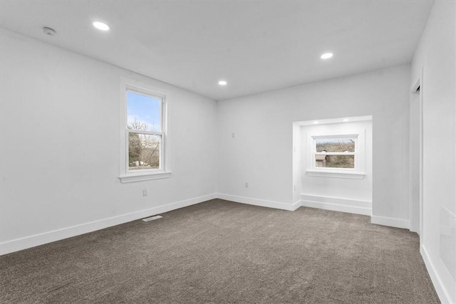 spare room with dark colored carpet, a healthy amount of sunlight, baseboards, and recessed lighting