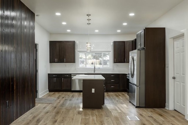 kitchen featuring a center island, stainless steel appliances, a sink, dark brown cabinets, and light wood-type flooring