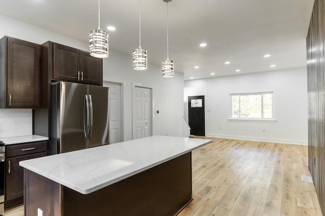 kitchen with a kitchen island, dark brown cabinets, freestanding refrigerator, decorative backsplash, and light wood finished floors