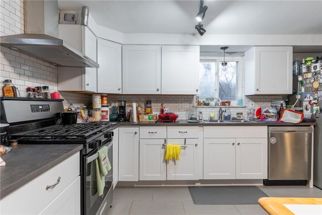 kitchen featuring a sink, white cabinets, appliances with stainless steel finishes, wall chimney range hood, and dark countertops