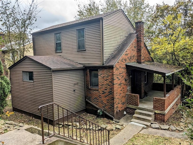 rear view of house featuring roof with shingles, brick siding, a chimney, and a porch