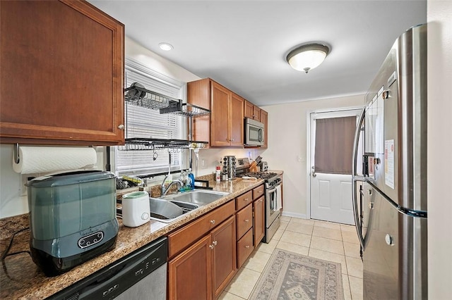 kitchen with brown cabinets, stainless steel appliances, light tile patterned flooring, a sink, and baseboards