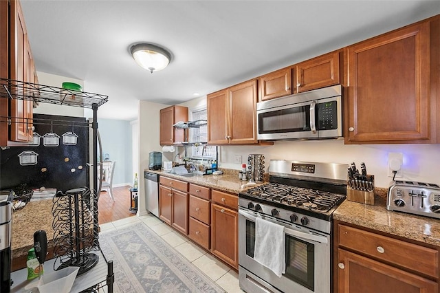 kitchen featuring baseboards, brown cabinetry, appliances with stainless steel finishes, a sink, and light tile patterned flooring