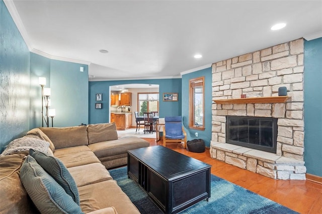 living area featuring recessed lighting, ornamental molding, a stone fireplace, wood finished floors, and baseboards