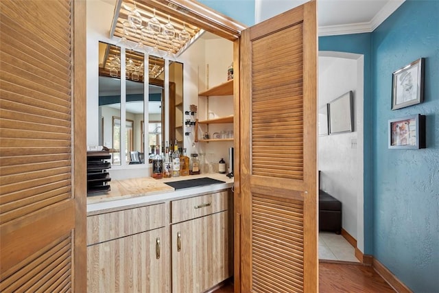 bar featuring a dry bar, a textured wall, ornamental molding, wood finished floors, and baseboards