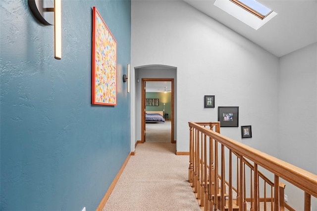 hall featuring arched walkways, light carpet, an upstairs landing, baseboards, and lofted ceiling with skylight