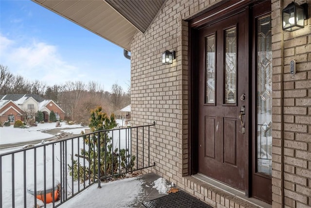 snow covered property entrance featuring brick siding and a balcony