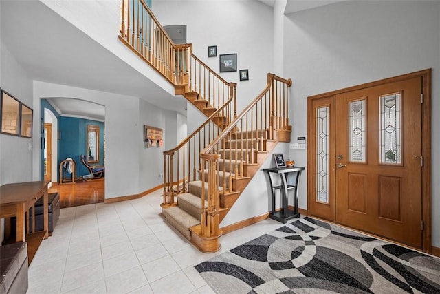 foyer entrance featuring arched walkways, tile patterned flooring, a high ceiling, baseboards, and stairs