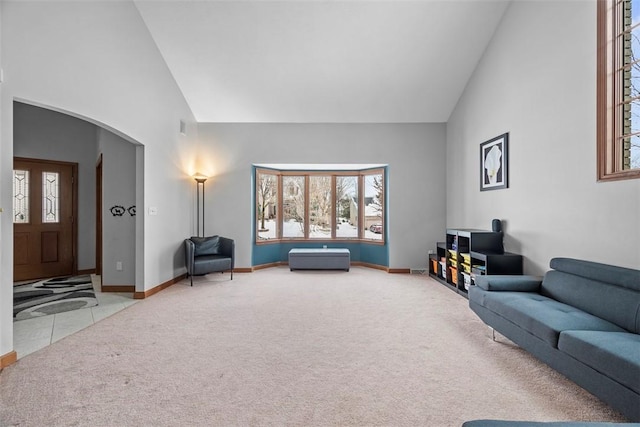 carpeted living area featuring arched walkways, high vaulted ceiling, and baseboards